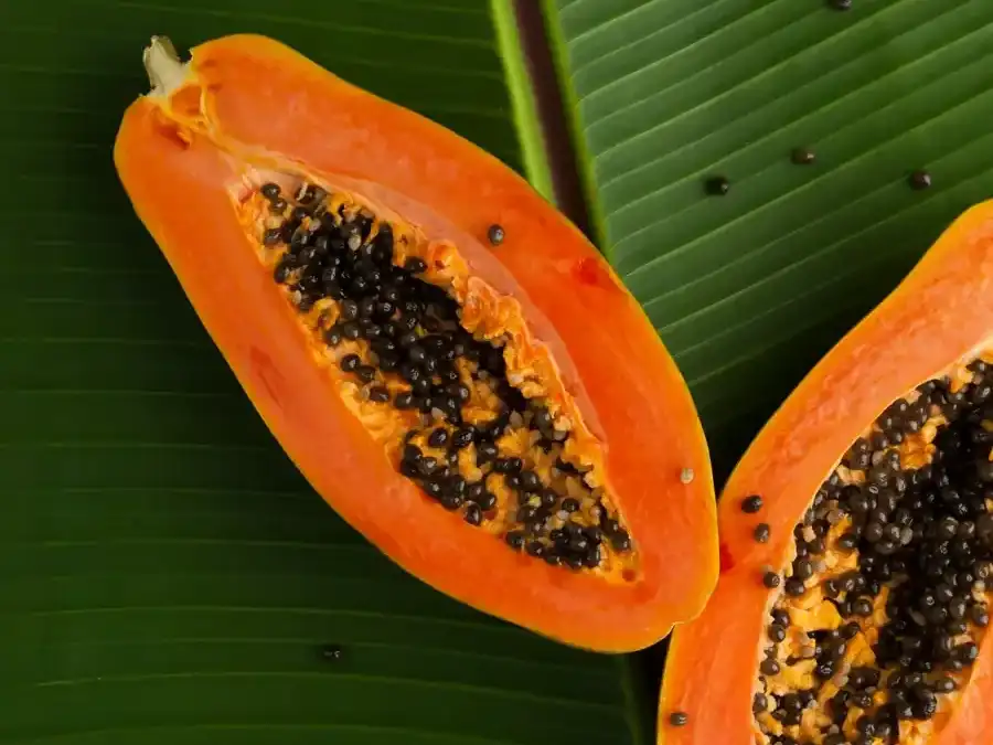 A halved papaya on a green banana leaf