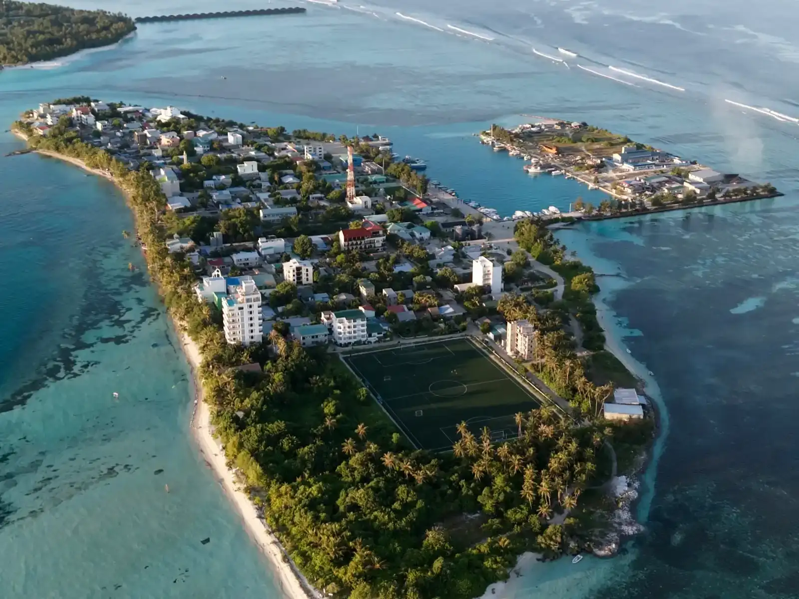 Aerial view of Dhiffushi in early morning light, with the village, harbour and football ground inside a wide turquoise lagoon