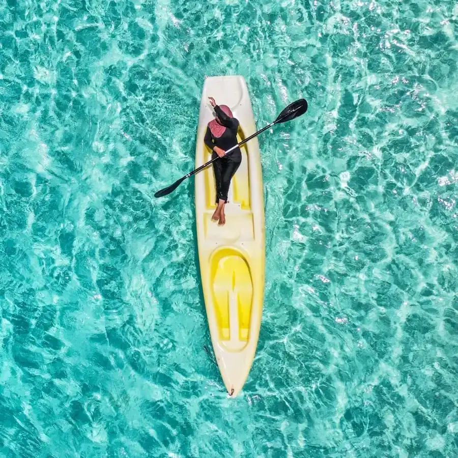 A person paddling a yellow kayak over clear turquoise water, seen from above