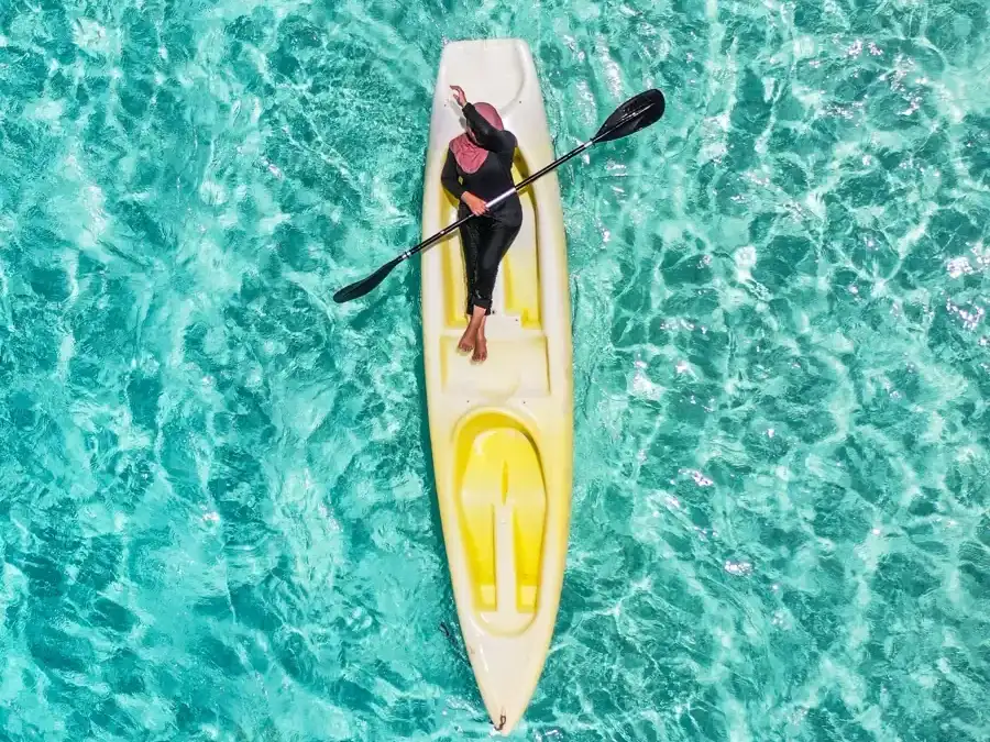 A person paddling a yellow kayak over clear turquoise water, seen from above