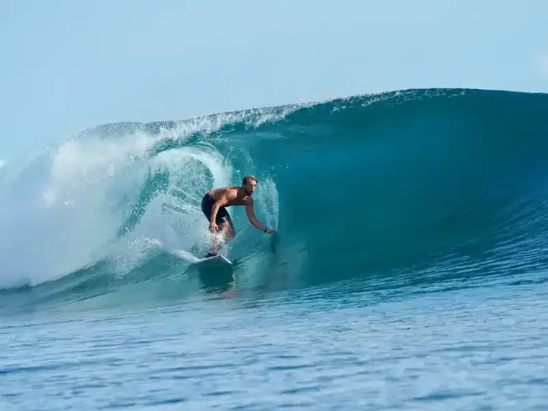 A surfer riding inside a curling blue wave